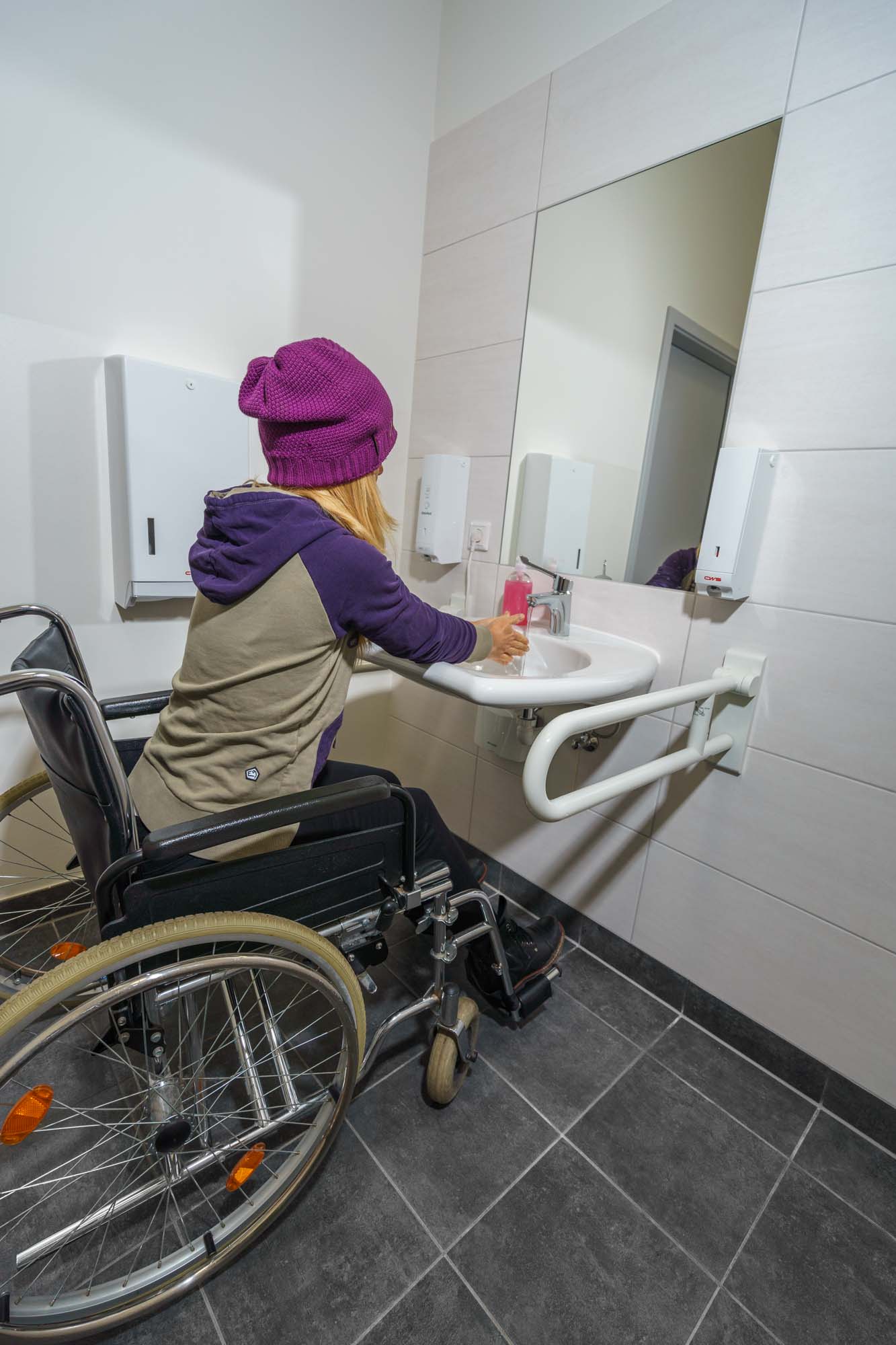 Frau im Rollstuhl beim Händewaschen im Behindertengerechten WC.