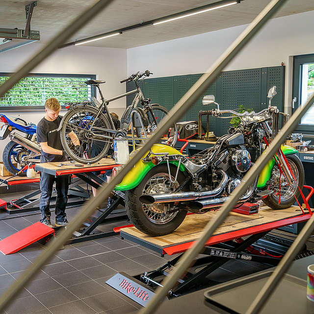 Eine Werkstatt mit im Hintergrund zu sehenden Hebebühnen für Zweiräder.